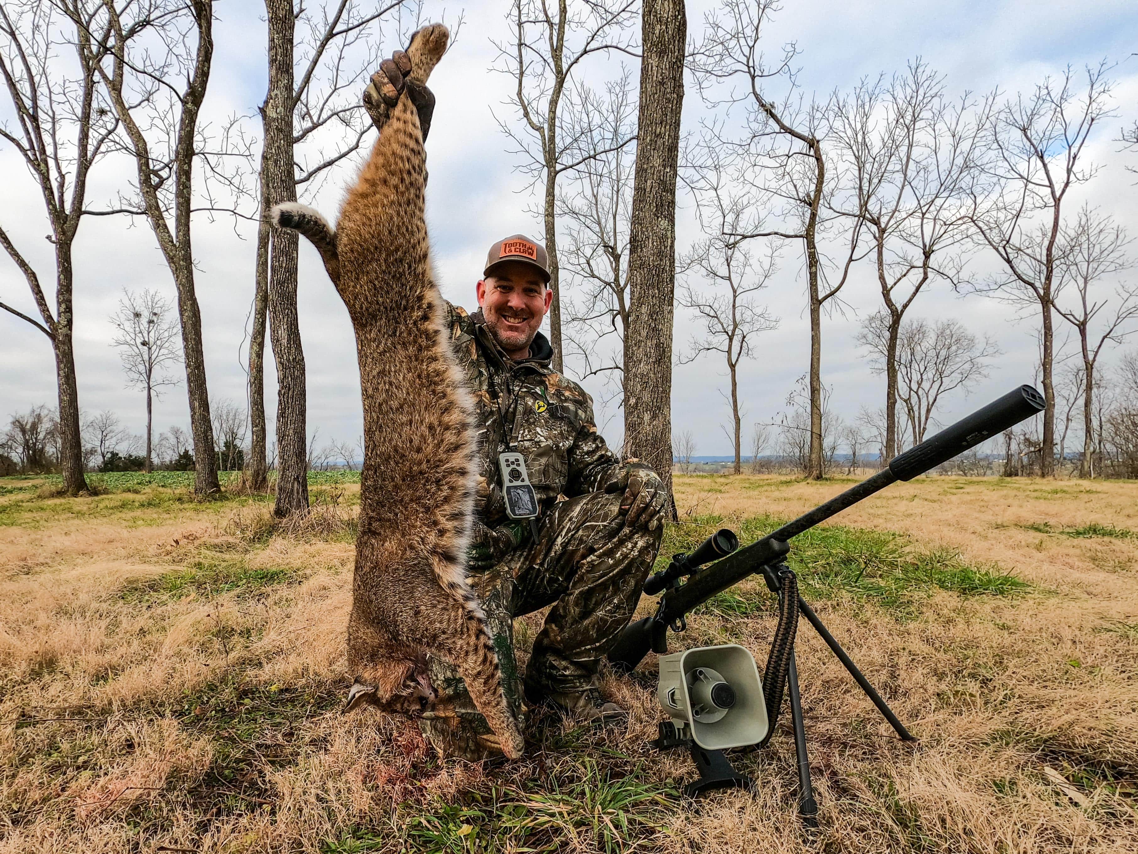jon collins posing with a bobcat an x24 foxpro game call and a rifle